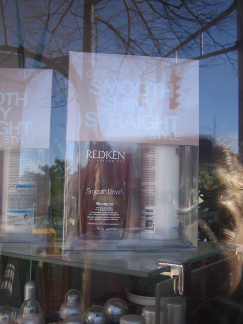 A double exposed image that appears to be a sign on top of some hair projects in a shop. You can see the sky in the background of the double exposure.