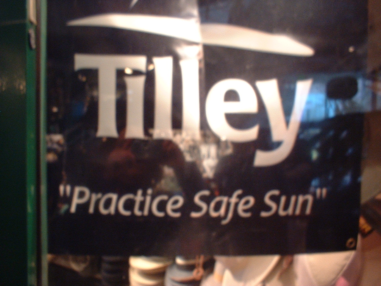 A black sign that says 'Tilley, Practice Safe Sun' in white letters. Appears to be on a glass window of a cafe.
